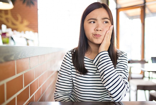 Woman with striped shirt rubbing tooth in pain