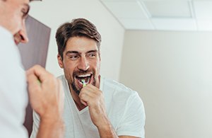 Man in white shirt brushing his teeth in the mirror