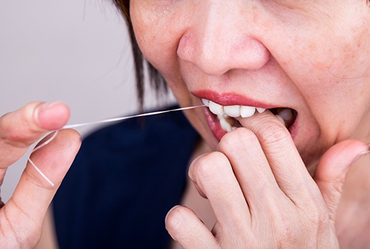 A person using dental floss to remove a lodged object between their teeth causing pain