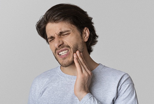 A younger male wearing a gray shirt and holding his jaw while cringing in pain