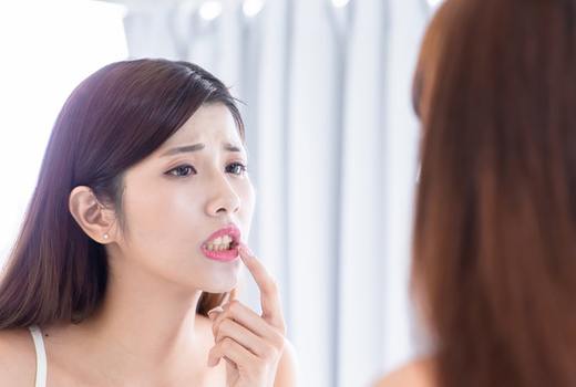 Woman examining her lips in the mirror with concern