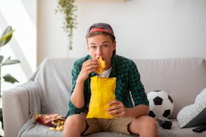 teenager watching football eating unhealthy food 