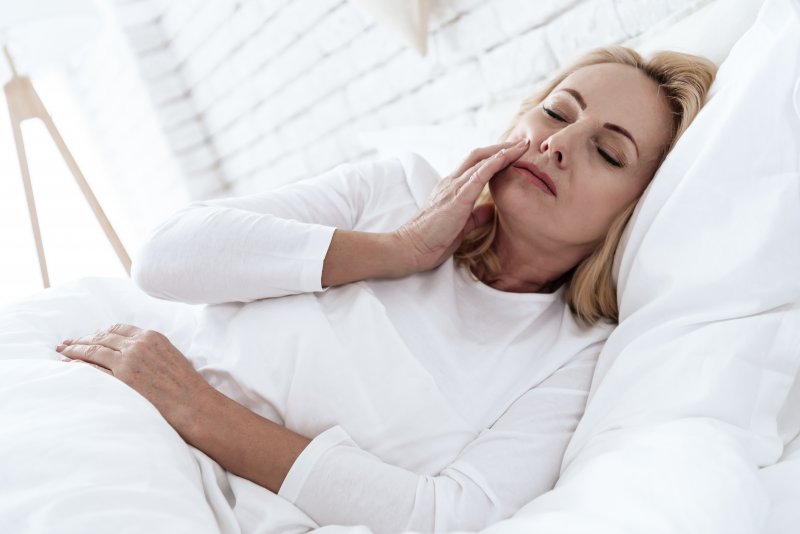 A woman in bed rubbing her jaw due to teeth grinding