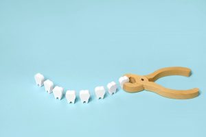 A row of toy wooden teeth with toy forceps pulling one