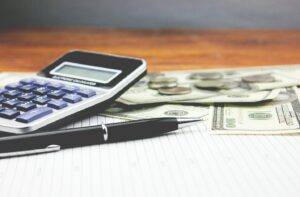 Calculator and pen pictured next to dollars and cents.